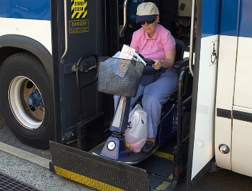 A person with a mobility scooter getting off of a bus.