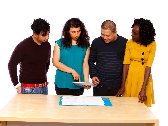 4 people standing together and looking at information on a tablet.