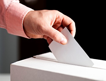 A person putting a ballot paper into a ballot box.