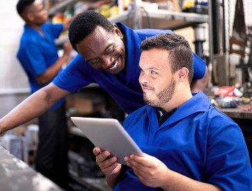 2 people in a workshop talking to each other. One is holding a tablet.