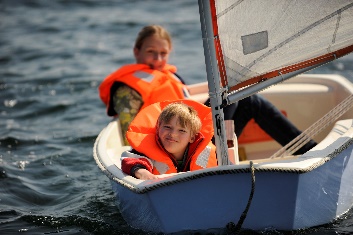 A child in a small sailing boat on the water with a supervisor.