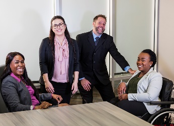 A group of people sitting and standing together in an office. 