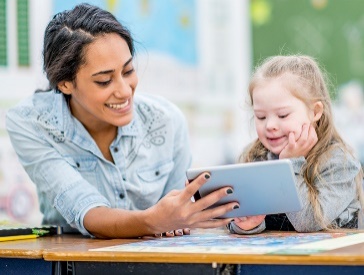 A teacher helping a child using a tablet.